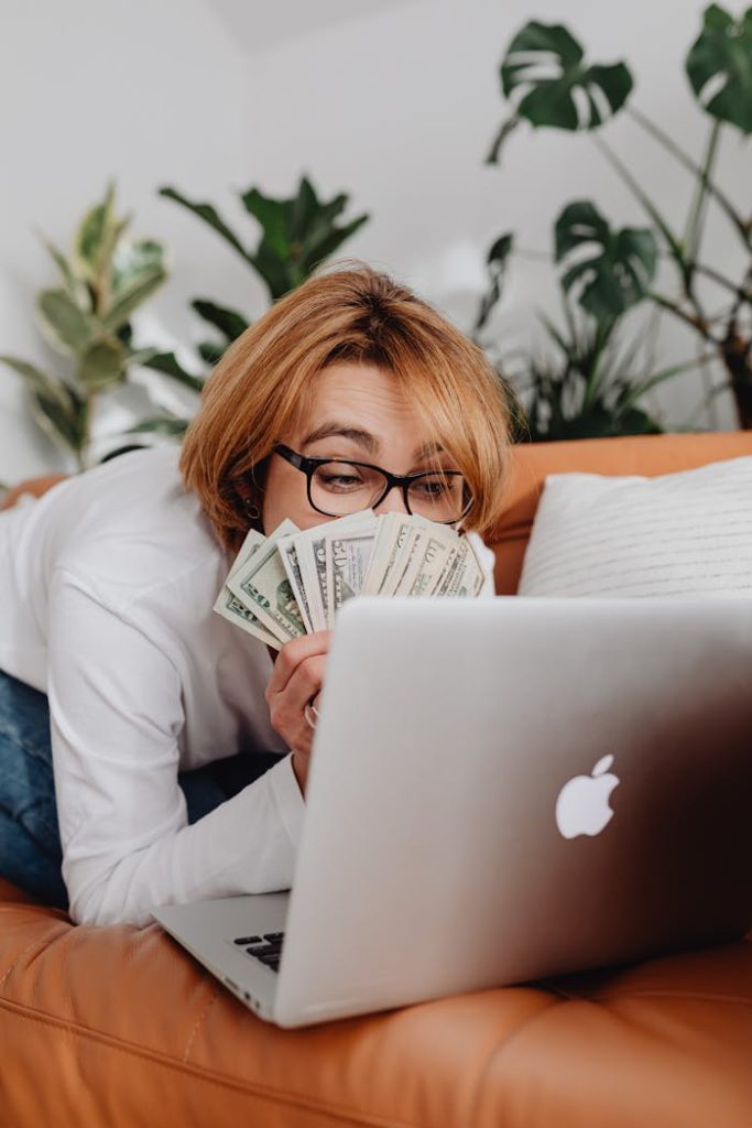 Woman Sitting in front of a Laptop and Covering Half of Her Face with Cash